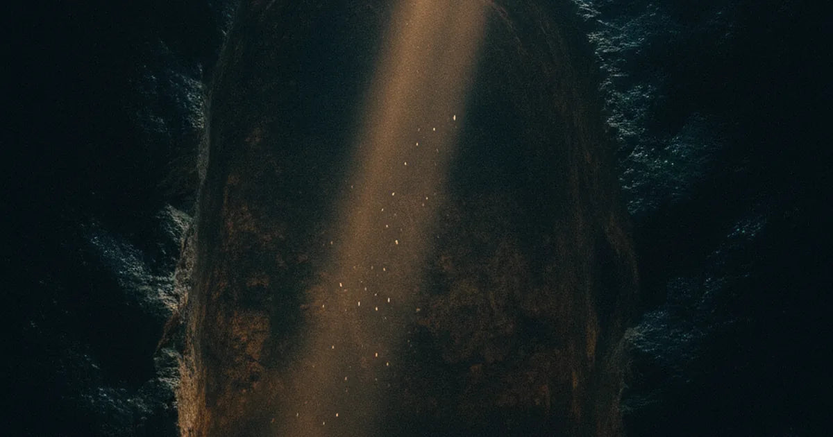 Nicchia di roccia vuota illuminata da un raggio di luce dorata, con candele votive nell'ombra sottostante.